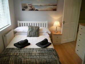 Ein Schlafzimmer mit einem Bett, einem Nachttisch mit Lampe, einem Gemälde an der Wand und einer Tür.