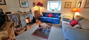 A cozy living room with a fireplace, a blue sofa, a grey sofa, a wooden coffee table, and a bookshelf. - 3 Bed in Durness (oc-d545850) (Durness)