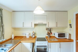 A compact kitchen with white cabinets, a stove, a microwave, and a kettle. - 3 Bed in Rockcliffe (oc-d545917) (Rockcliffe)