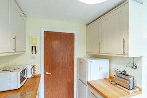 A compact kitchen with white cabinets, a wooden door, a microwave, a refrigerator, and a toaster. - 3 Bed in Rockcliffe (oc-d545917) (Rockcliffe)
