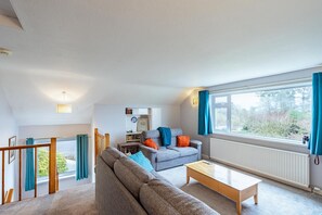 A modern living room with a sofa, coffee table, and a view of greenery outside. - 3 Bed in Rockcliffe (oc-d545917) (Rockcliffe)