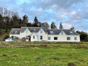 A white two-story house with a sloped roof, multiple windows, and a wooden fence in the foreground. - 8 Bed in New Galloway (oc-d594998) (New Galloway)