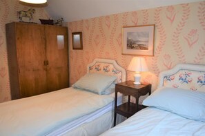 Un dormitorio con dos camas individuales, un armario de madera, una mesita de noche con lámpara y papel tapiz con motivos florales.