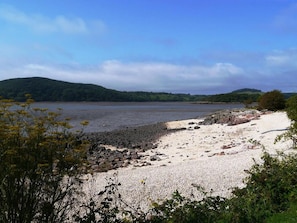 Un paisaje costero con una playa de guijarros, un litoral rocoso y colinas al fondo.