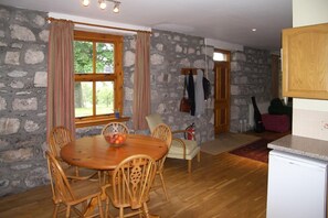 Ein Essbereich mit Holztisch und -stühlen, einer Steinwand und einem fenster mit Vorhängen.