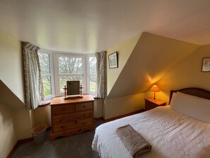 Ein Schlafzimmer mit Bett, Schminktisch, Nachttischlampe und einem fenster mit Vorhängen.