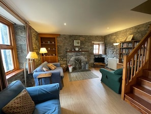 Ein gemütliches Wohnzimmer mit Kamin aus Stein, einer Bücherwand, einem Fernseher und einer Treppe.