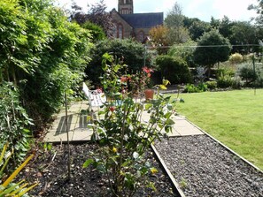 A garden with a bench, a rose bush, and a building in the background. - 3 Bed in Kirkcudbright (oc-d671636) (Kirkcudbright)