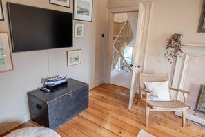 A living room with a flat-screen TV, a wicker chair, and a staircase leading to an upper level. - 3 Bed in Kirkcudbright (oc-d671636) (Kirkcudbright)