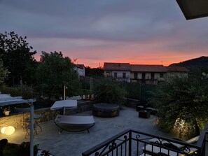 An outdoor patio area with a lounge chair, a table, and a small round table, surrounded by greenery and overlooking a hillside. - Villa located 5 minutes from the "Path of the Gods," ideal for visiting Amalfi and the Amalfi Coast (Pianillo)