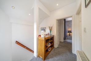 A hallway with a wooden staircase, a small wooden shelf with books and decorative items, and a door leading to another room. - 3 Bed in Crieff (oc-d672592) (Crieff)