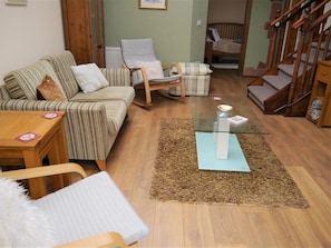 Ein Wohnzimmer mit einer Couch, einem Sessel, einem Glastisch und einem kleinen Beistelltisch mit Kissen.