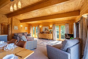 A wooden cabin interior with a dining area, sofa, and a kitchen area. - 3 Bed in Kippford (oc-d597989) (Kippford)
