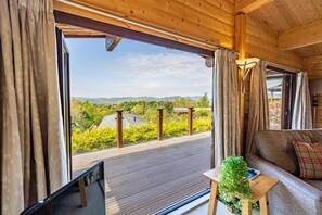 A room with a large window, a sofa, a small table, and a view of greenery and hills. - 3 Bed in Kippford (oc-d597989) (Kippford)