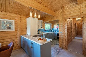 A log cabin interior with a kitchen area featuring a marble countertop, wooden cabinets, and pendant lighting. - 3 Bed in Kippford (oc-d597989) (Kippford)