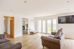 A spacious living room with a large sofa, a smaller armchair, and a television mounted on the wall. - 3 Bed in Dumfries (oc-d641667) (Torthorwald)