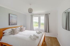 Ein Schlafzimmer mit einem großen Bett, einer Nachttischlampe, einem Bild an der Wand und Blick ins Freie durch ein Fenster.