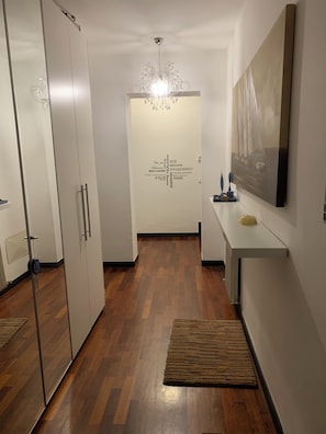 A hallway with a wooden floor, a chandelier, a wall-mounted painting, and a door with a welcome sign. - Experience Genoa: A Charming Apartment in the Heart of Its Historic Center (Genova)