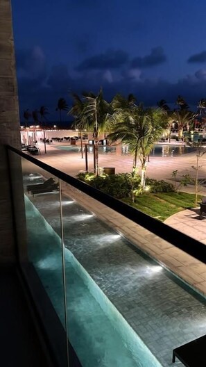 A nighttime view of a hotel pool area with palm trees and a paved walkway.