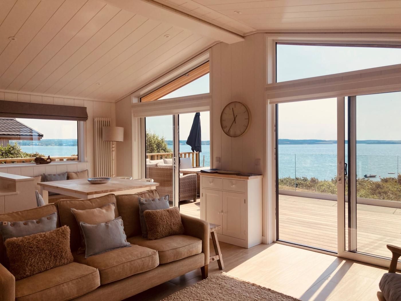 Un interior moderno con sofá, mesa de comedor y zona de cocina, con ventanas amplias y vistas al mar.