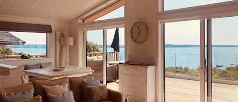 Un interior moderno con sofá, mesa de comedor y zona de cocina, con ventanas amplias y vistas al mar.