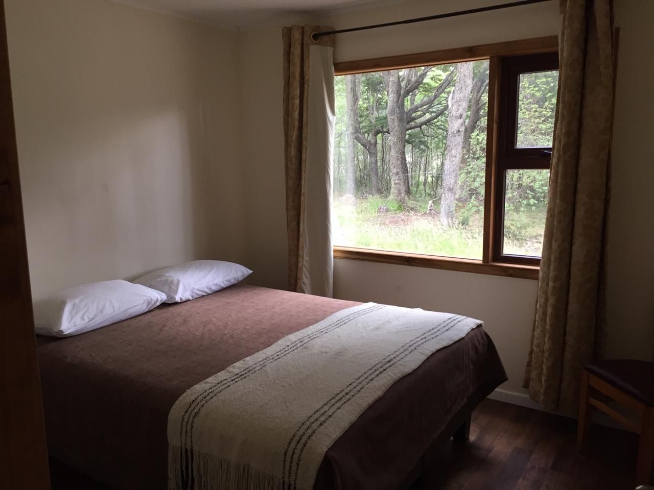 A bedroom with a single bed, a window with curtains, and a view of a forest.