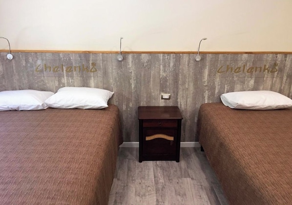 A room with two beds, each with a wooden headboard and a small bedside table.