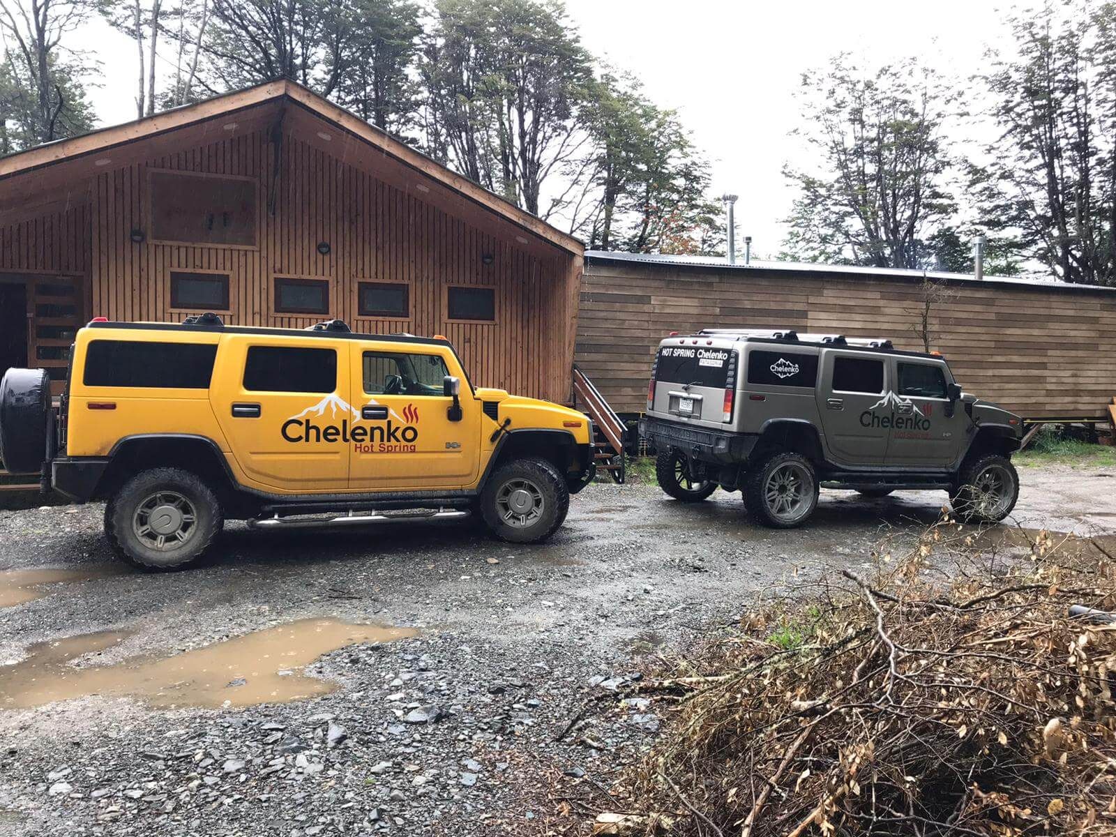 Two vehicles parked in front of a wooden building with a gravel ground.