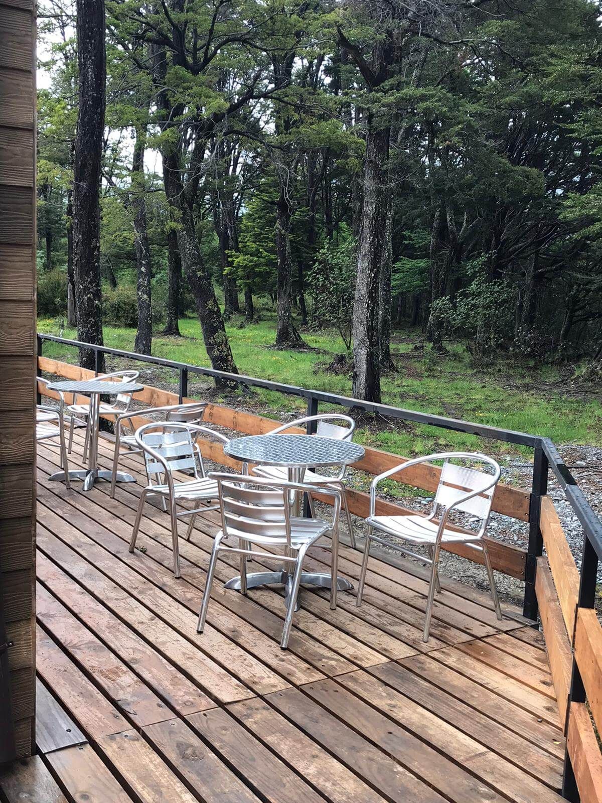 Une terrasse extérieure avec des tables et des chaises en métal, entourée d’une forêt.