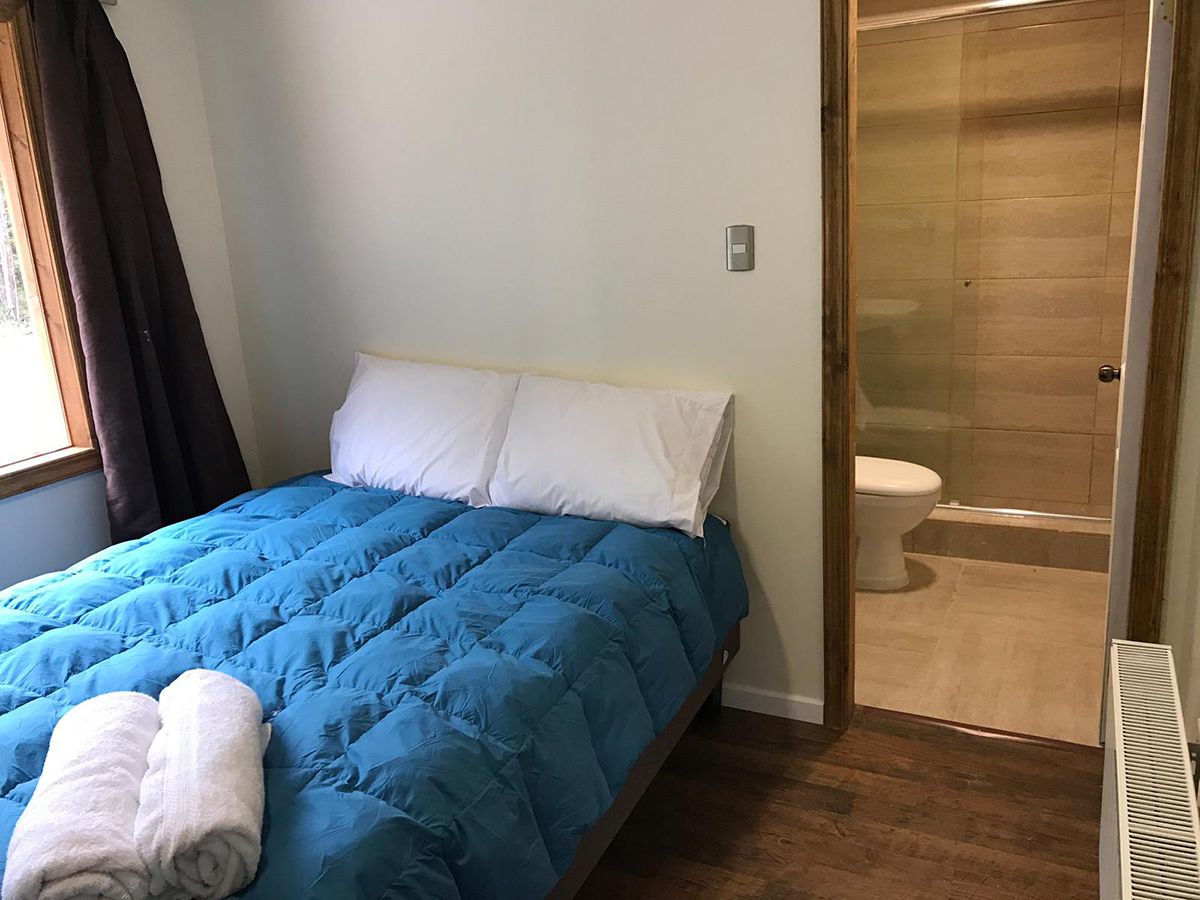 Une chambre à coucher avec un lit, un oreiller blanc, une couverture bleue, une serviette, un plancher en bois, des toilettes blanches et un espace douche.