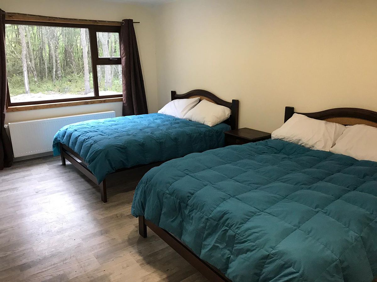 A bedroom with two beds, a window with curtains, and a radiator.