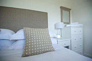 A neatly made bed with white linens and a patterned pillow, a bedside lamp, and a white dresser with drawers.
