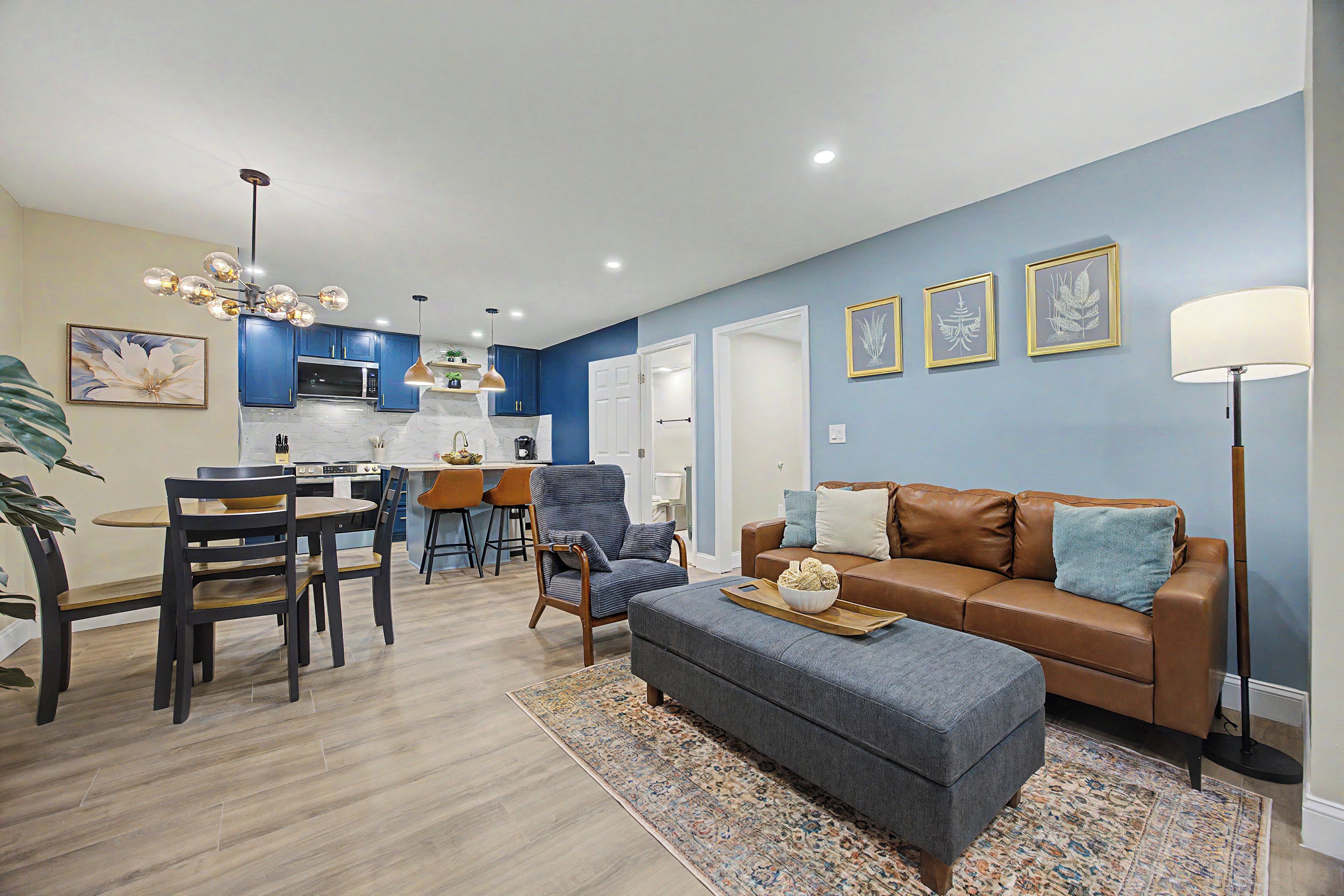 A modern living room with a brown leather sofa, a blue armchair, and a dining area with a wooden table and chairs.