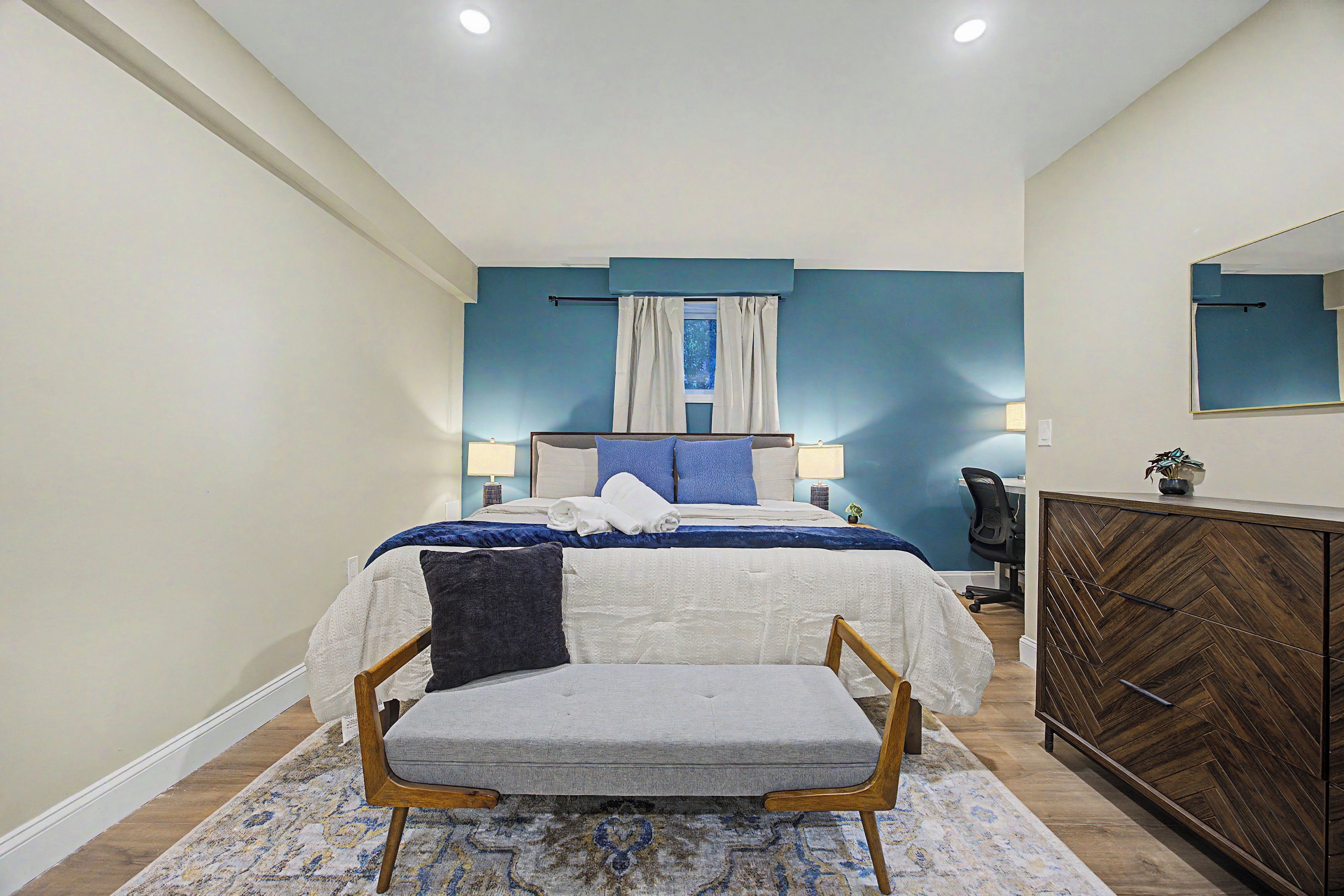 A bedroom with a bed, bedside tables, a chair, a dresser, and a mirror.