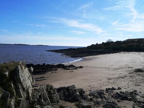 A beach with a rocky shoreline, a clear sky, and a distant view of land. - 3 Bed in Mossyard, Gatehouse Of Fleet (oc-d555706) (Gatehouse of Fleet)