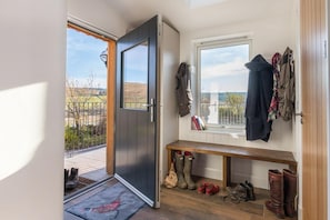 Una habitación con una puerta que da a un balcón, un banco con botas y una ventana con ropa colgada.