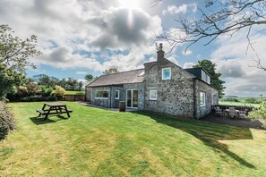 A stone house with a grassy yard, a picnic table, and a view of the countryside. - 4 Bed in Kirkcudbright (oc-d622412) (Kirkcudbright)