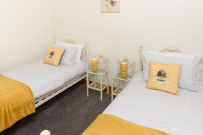 Camera doppia con due letti, ognuno con un cuscino decorato con un motivo a ape, un comodino con una lampada e una piccola decorazione a parete.
