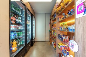 A narrow aisle with refrigerated beverage dispensers on the left and shelves stocked with snacks and packaged goods on the right. - Lorena 908 · Urban Retreat with Pool in Jardim Paulista (São Paulo)