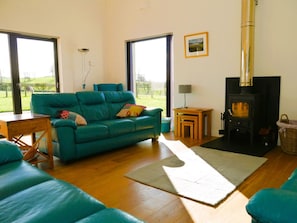 A living room with a teal sofa, a wooden coffee table, a fireplace, and a view of the outdoors. - 4 Bed in Castle Douglas (oc-d637110) (Rhonehouse)