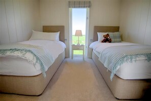 A hotel room with two single beds, a nightstand with a lamp, and a window with a view of the outdoors. - 3 Bed in Mossyard, Gatehouse Of Fleet (oc-d546163) (Gatehouse of Fleet)