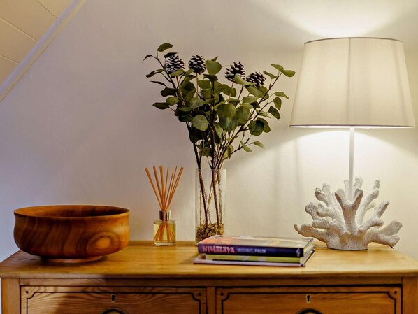 Een houten nachtkastje met een schaal, een vaas met groene bladeren, een lamp en een koraal sculptuur.