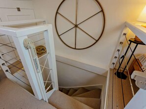 Eine Treppe mit einer weißen Tür, einem kreisförmigen Objekt an der Wand und einem schwarzen Metallständer mit einer Lampe.