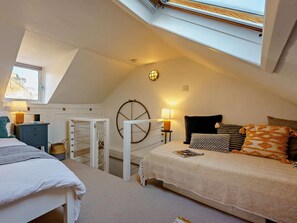 Een slaapkamer met een schuine plafond, dakraam, een bed met veel kussens, een nachtkastje met een lamp en een kleine stoel.