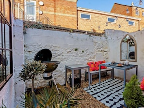 Een terras met een barbecue, een tafel met stoelen en een decoratief vloerkleed.