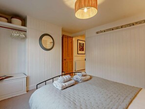 Ein Schlafzimmer mit einem Bett, einem Nachttisch, einem Spiegel, einem Kleiderschrank und einer Tür zu einem anderen Raum.