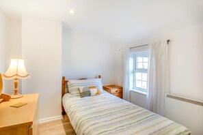 A small, neatly arranged bedroom with a single bed, a bedside table with a lamp, a window with curtains, and a radiator. - 2 Bed in Grafham (oc-w45994) (Grafham)