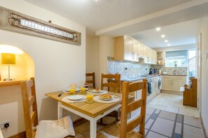A dining area with a table set for two, a kitchen in the background, and a visible power outlet on the wall. - 2 Bed in Grafham (oc-w45994) (Grafham)