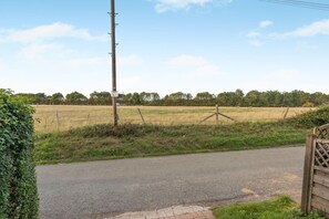 Un camino rural con una verja de madera, un poste de electricidad y un campo al fondo.