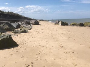 Ein sandiger Strand mit großen Felsen und blauem Himmel.